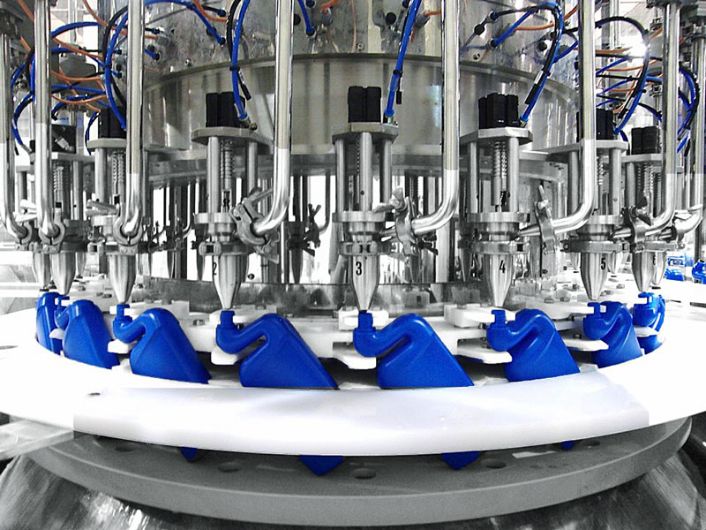 Rotary liquid filling machines with multiple stainless steel nozzles filling blue duck-shaped plastic bottles on an automated production line.