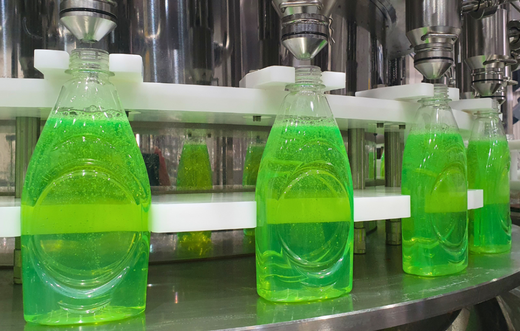 Close-up of rotary volumetric filling nozzles dosing liquid into clear containers